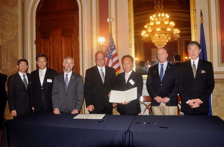 Seven men standing at a table with a signed agreement