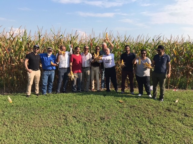 group of people posing for a photo in front of a corn field