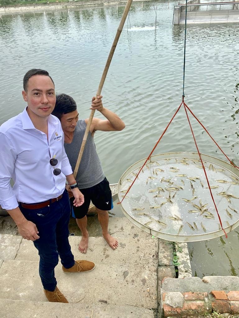 Vietnam Aquaculture- 2 men standing on steps, one holding a bamboo stick with with a circle filled with fish that have been collected from the water