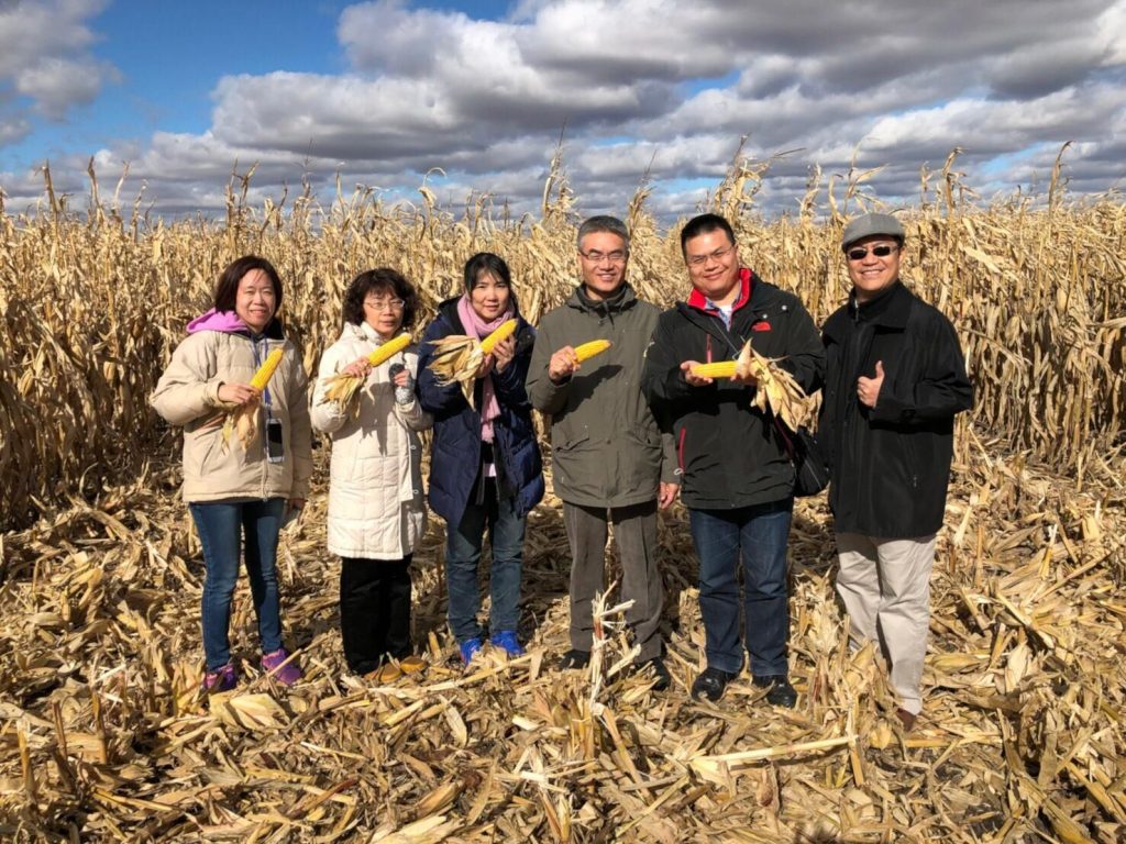 2018 Taiwan ExEx Team- team members standing in a field of corn holding ears of corn