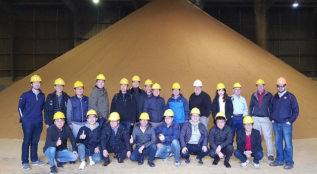 Korea ExEx 2018- group photo of team members standing in front of a large mound of DDGS
