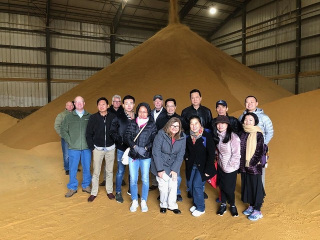 SEA ExEx Team- group photo of team members standing in a storage facility in front of a large mound of DDGS
