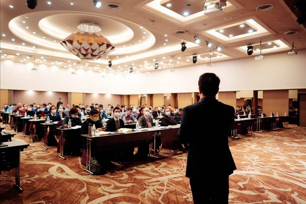 Man Standing In front of Large Sitting Crowd