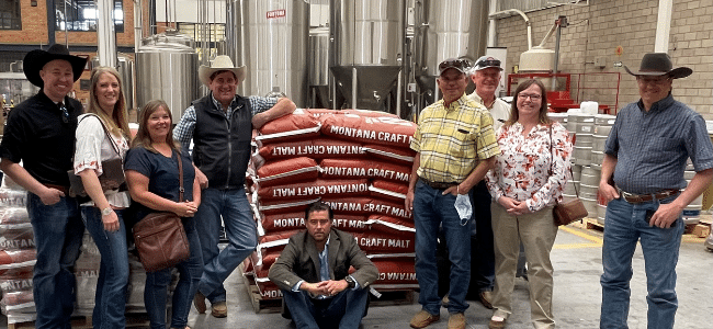 a group of people standing in a brewery with bags of malt
