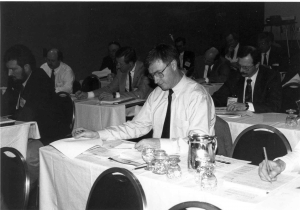 A black and white photo focused on a man reading a document in a conference room